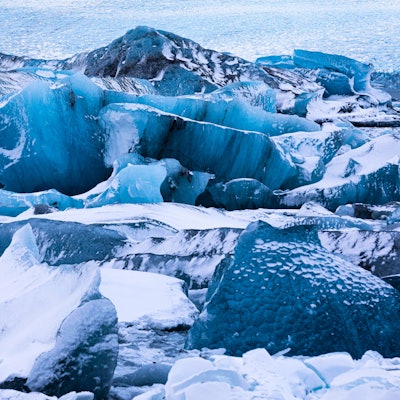 Verschneite Eisberge in der Gletscherlagune Jökullsarlon auf Island, dahinter der Breidamerkurjökull. Hier ist eine Eishöhle eingestürzt.