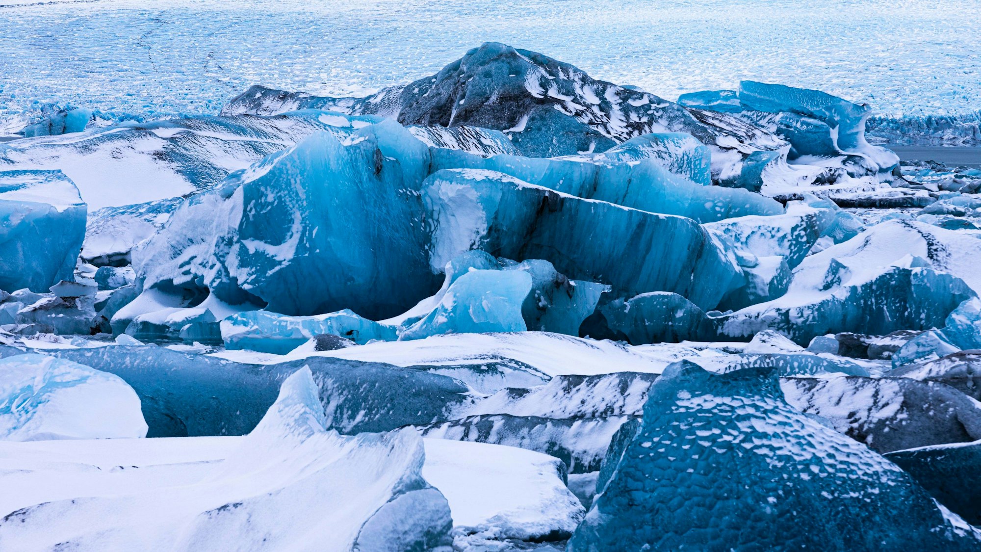 Verschneite Eisberge in der Gletscherlagune Jökullsarlon auf Island, dahinter der Breidamerkurjökull. Hier ist eine Eishöhle eingestürzt.