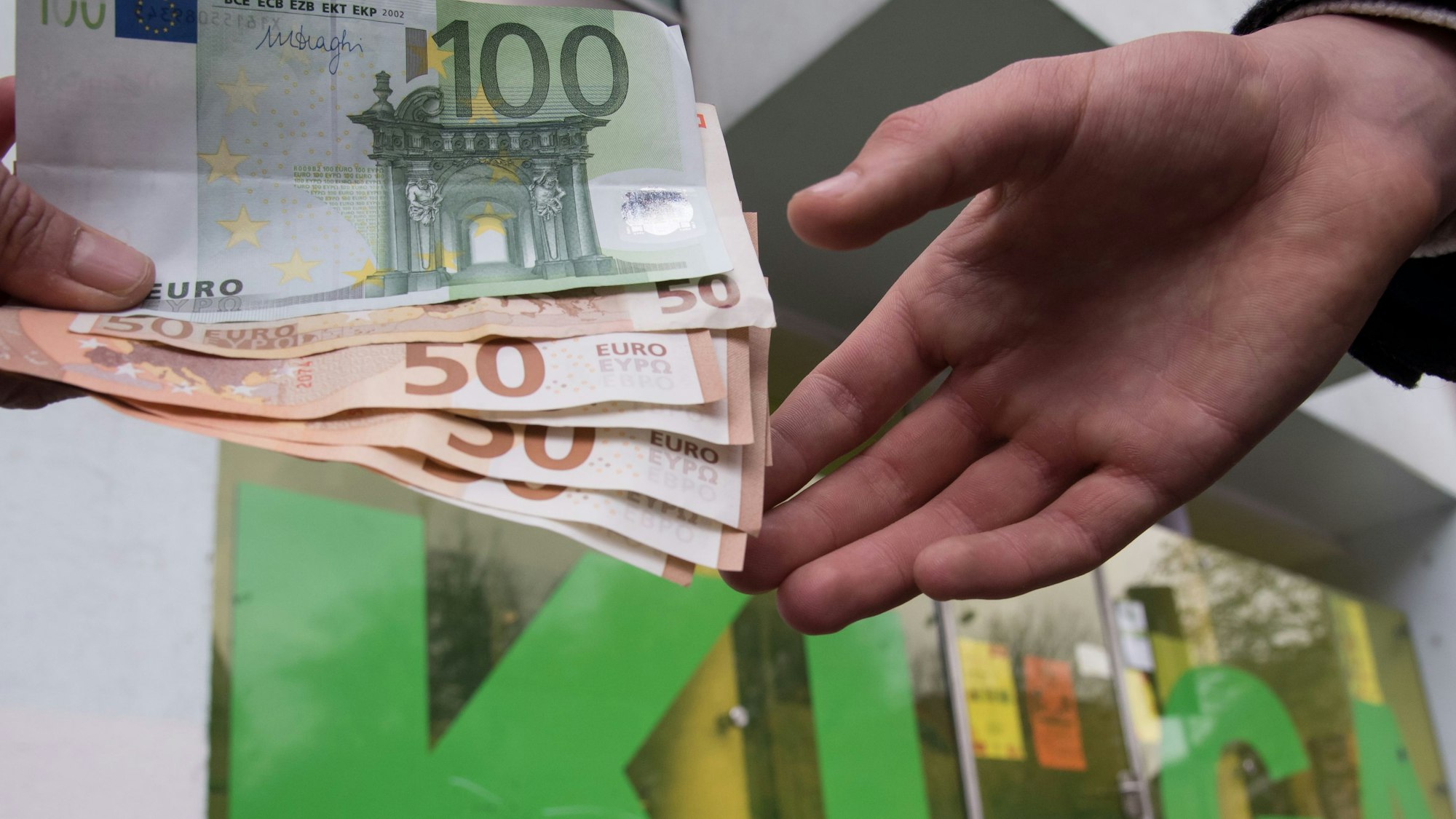 Ein Mann und eine Frau halten mehrere Geldscheine vor einem Kindergarten in den Händen.