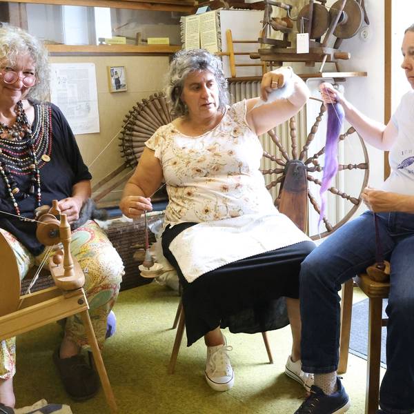 Die drei Frauen sitzen nebeneinander. Doris Schmitten bedient ein Spinnrad, ihre Mitstreiterinnen halten Fäden in den Händen.