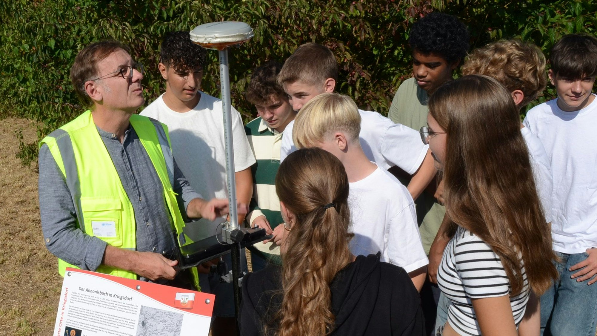 Ein Mann in gelber Warnweste, Schülerinnen und Schüler stehen um ein elektronisches Messgerät herum.