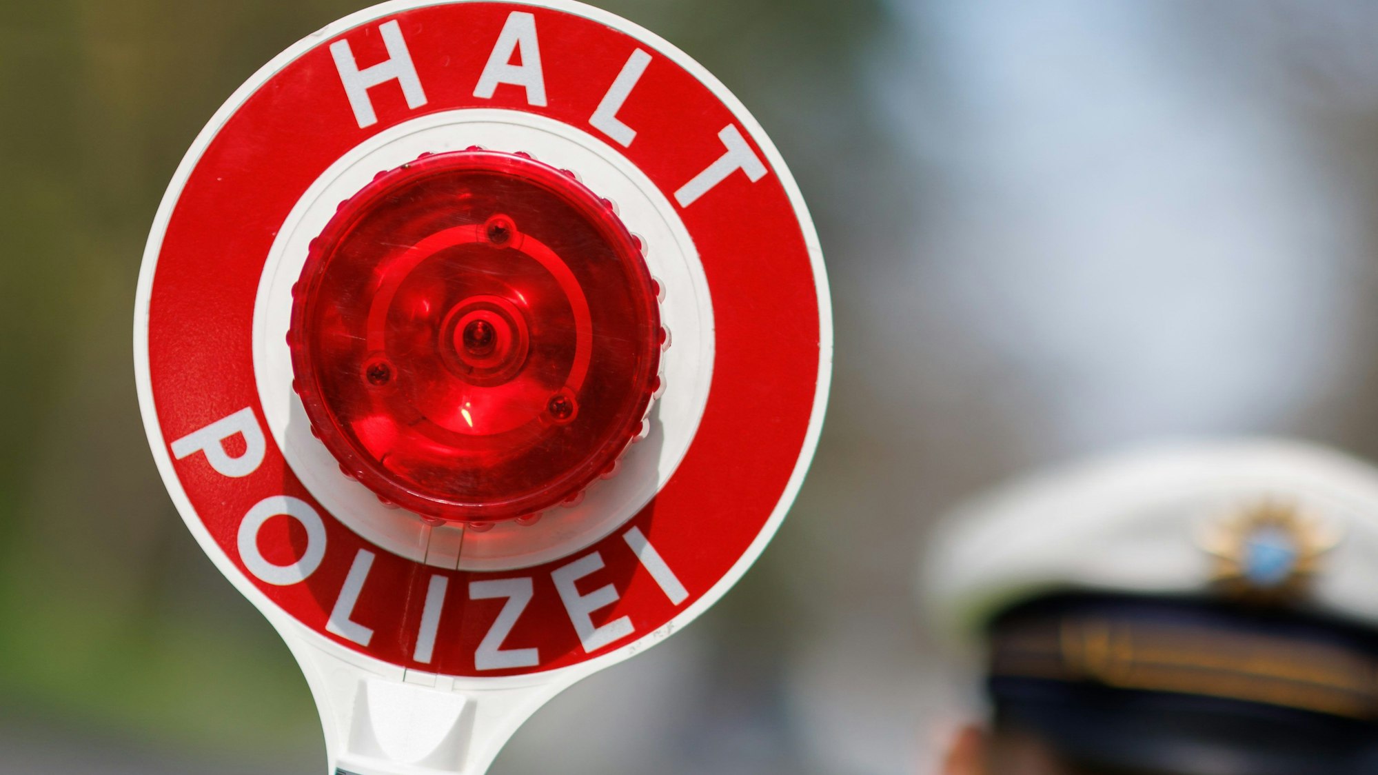 Auf dem Bild ist zu sehen, wie ein Polizist eine Kelle mit Stoppsignal hoch hält.