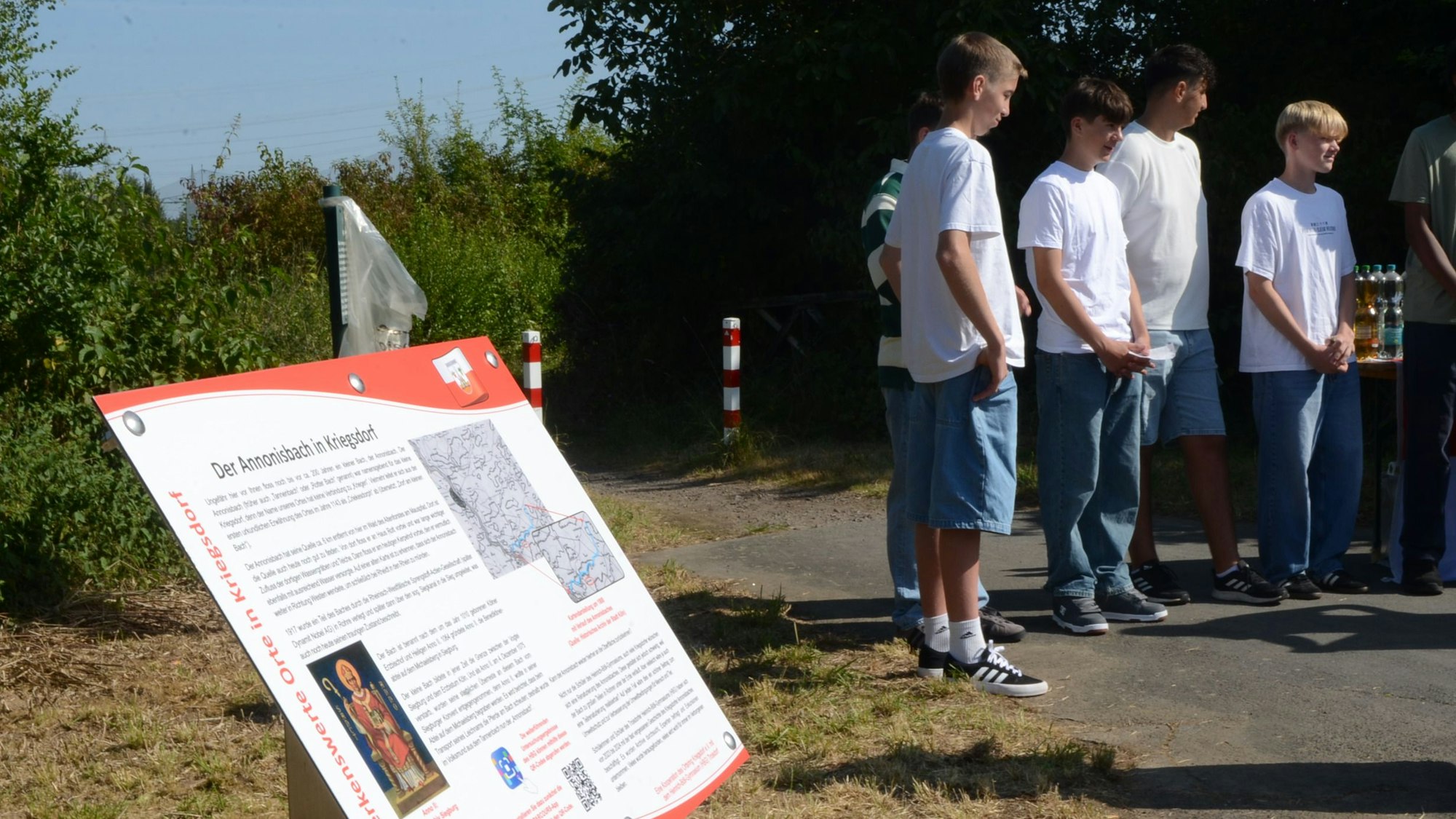 Eine Schautafel mit der Überschrift „Der Annonisbach in Kriegsdorf“. Im Hintergrund stehen Schüler.