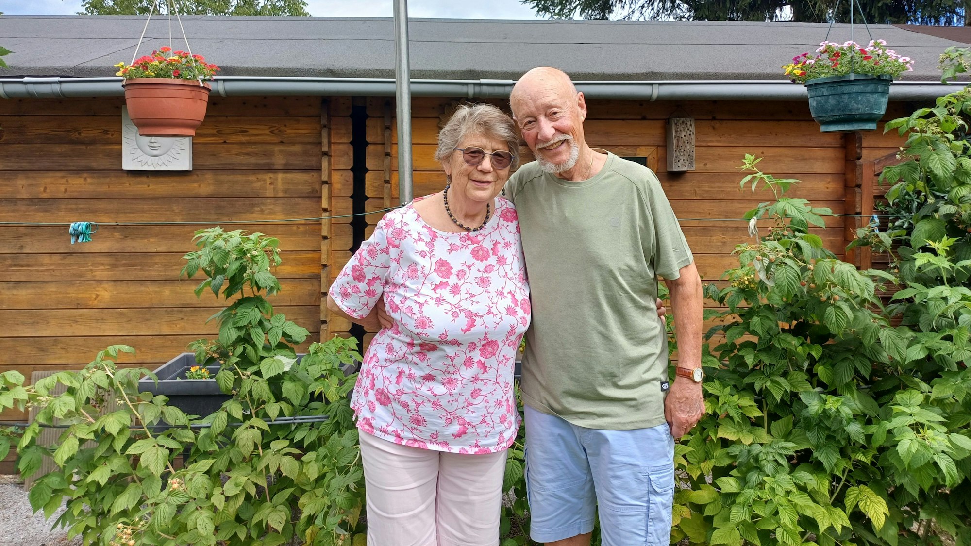 Ein Mann und eine Frau stehen in einem Garten vor einer Laube.