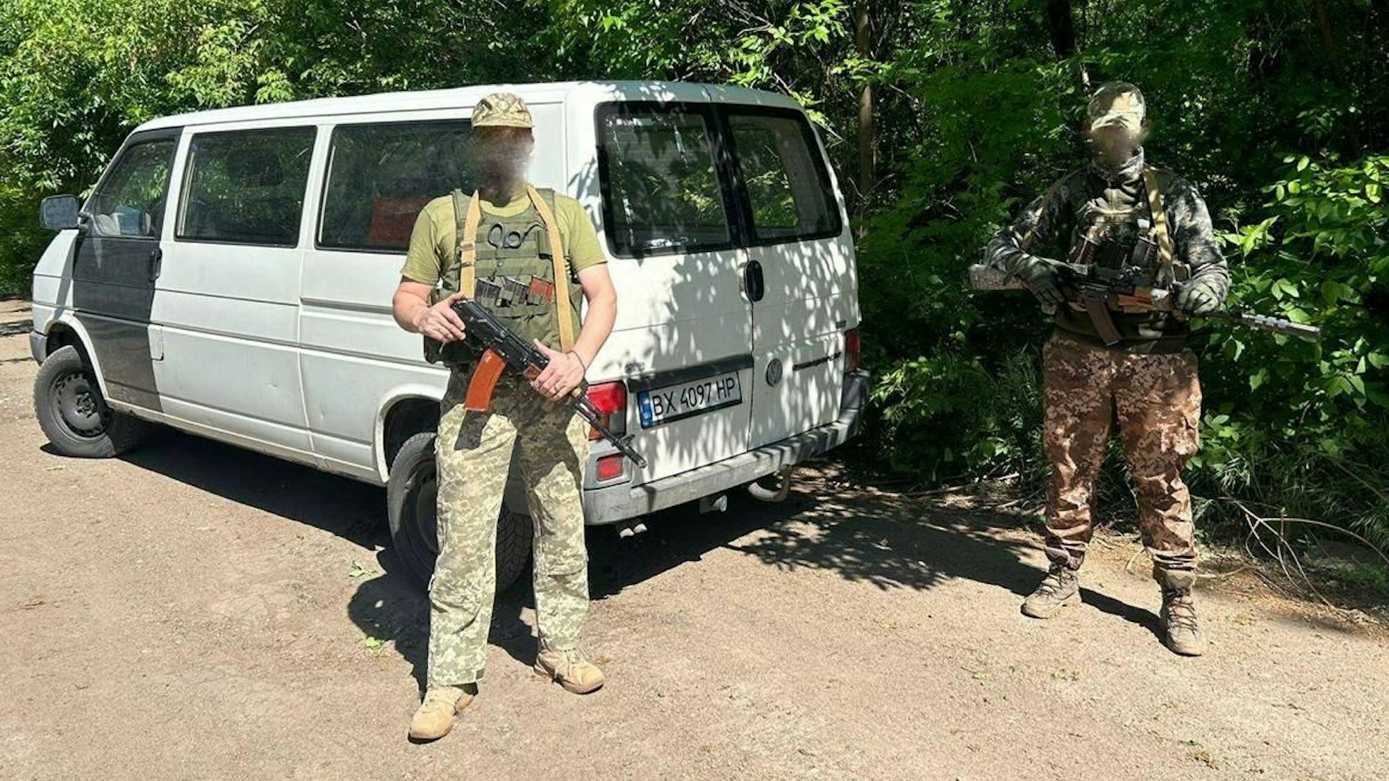 Zwei bewaffnete Ukrainer stehen vor einem VW-Bus.