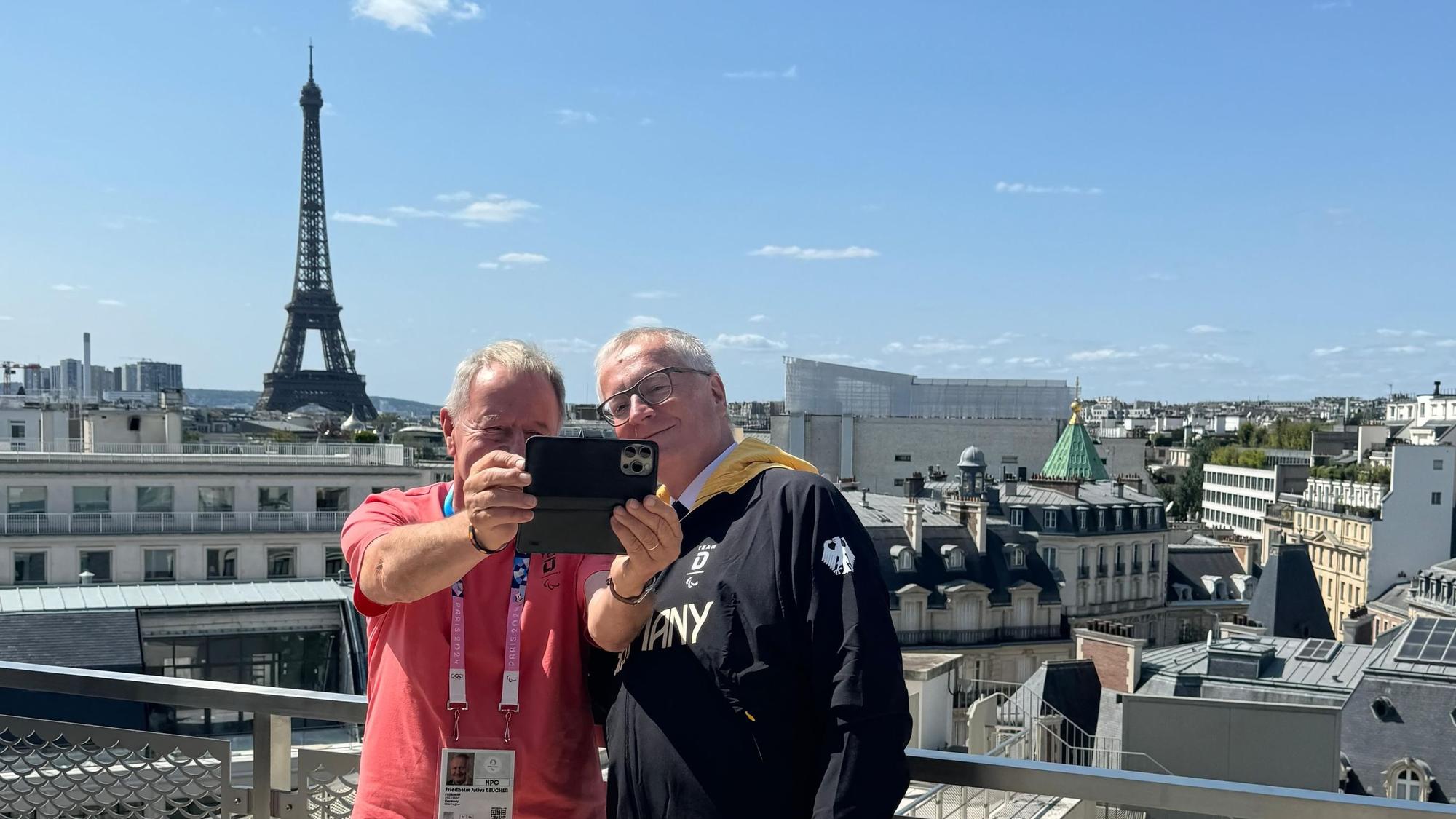 Zwei Männer machen im Rahmen der Paralympics in Paris ein Selfie mit dem Eiffelturm im Hintergrund.