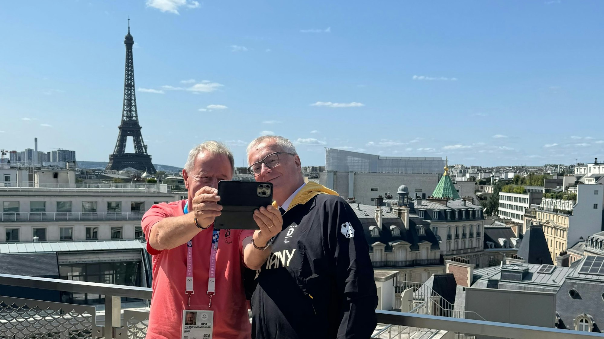 Zwei Männer machen im Rahmen der Paralympics in Paris ein Selfie mit dem Eiffelturm im Hintergrund.