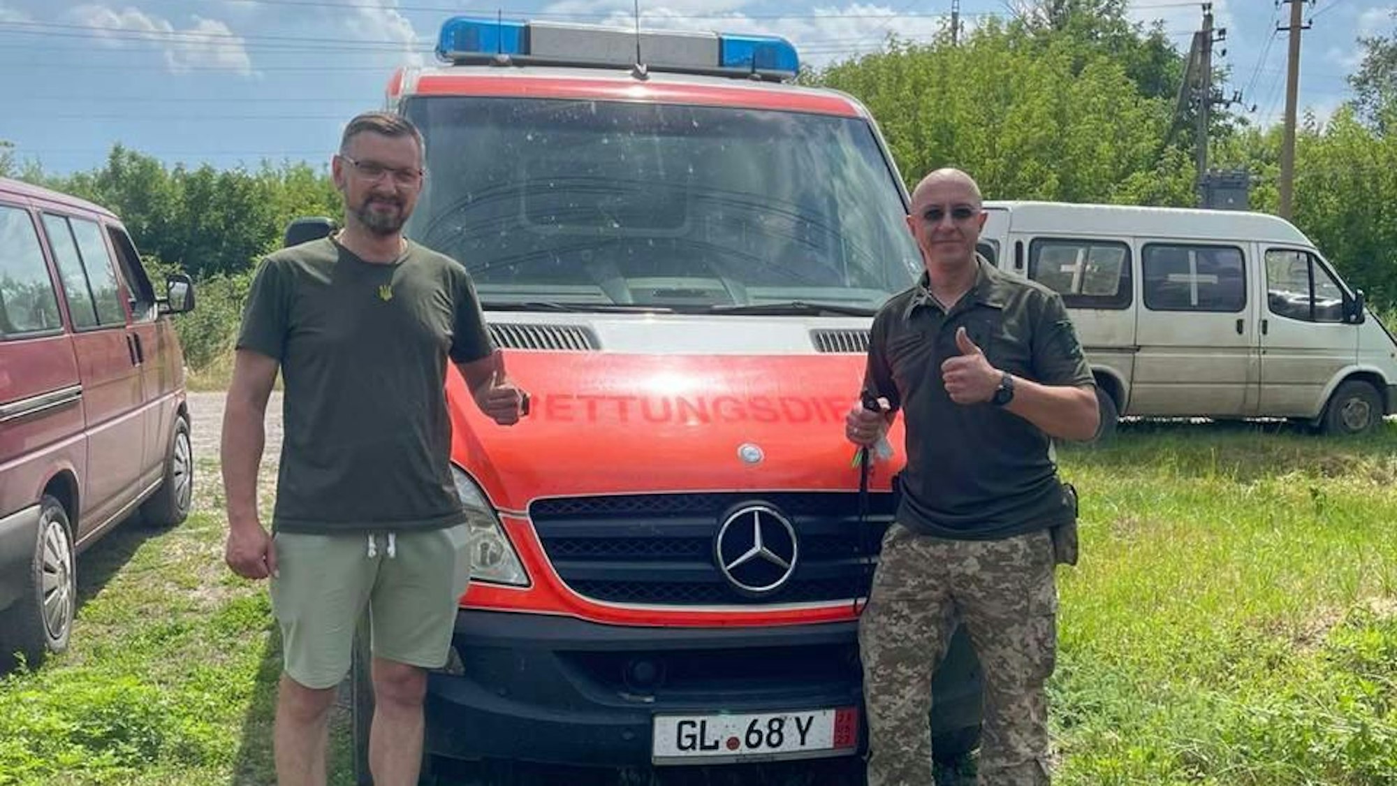 zwei Männer stehen vor einem Krankenwagen und strecken den Daumen in die Höhe.