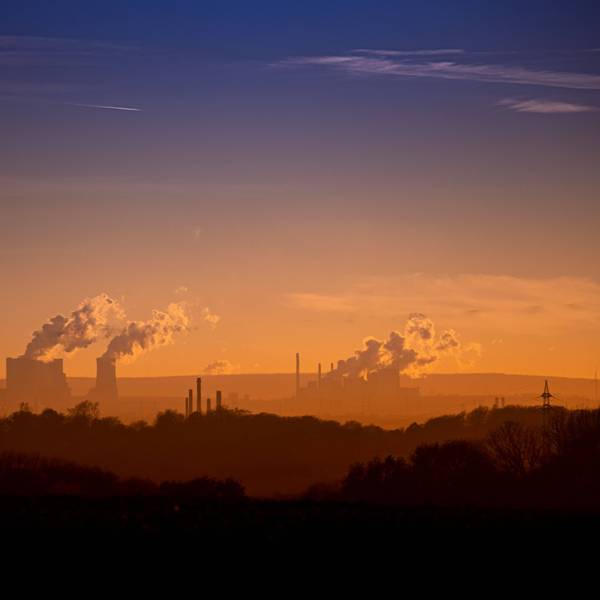 Blick auf das rheinische Braunkohlerevier in orangem Licht, mit Industrieschornsteinen und Rauch, der in den Himmel steigt.