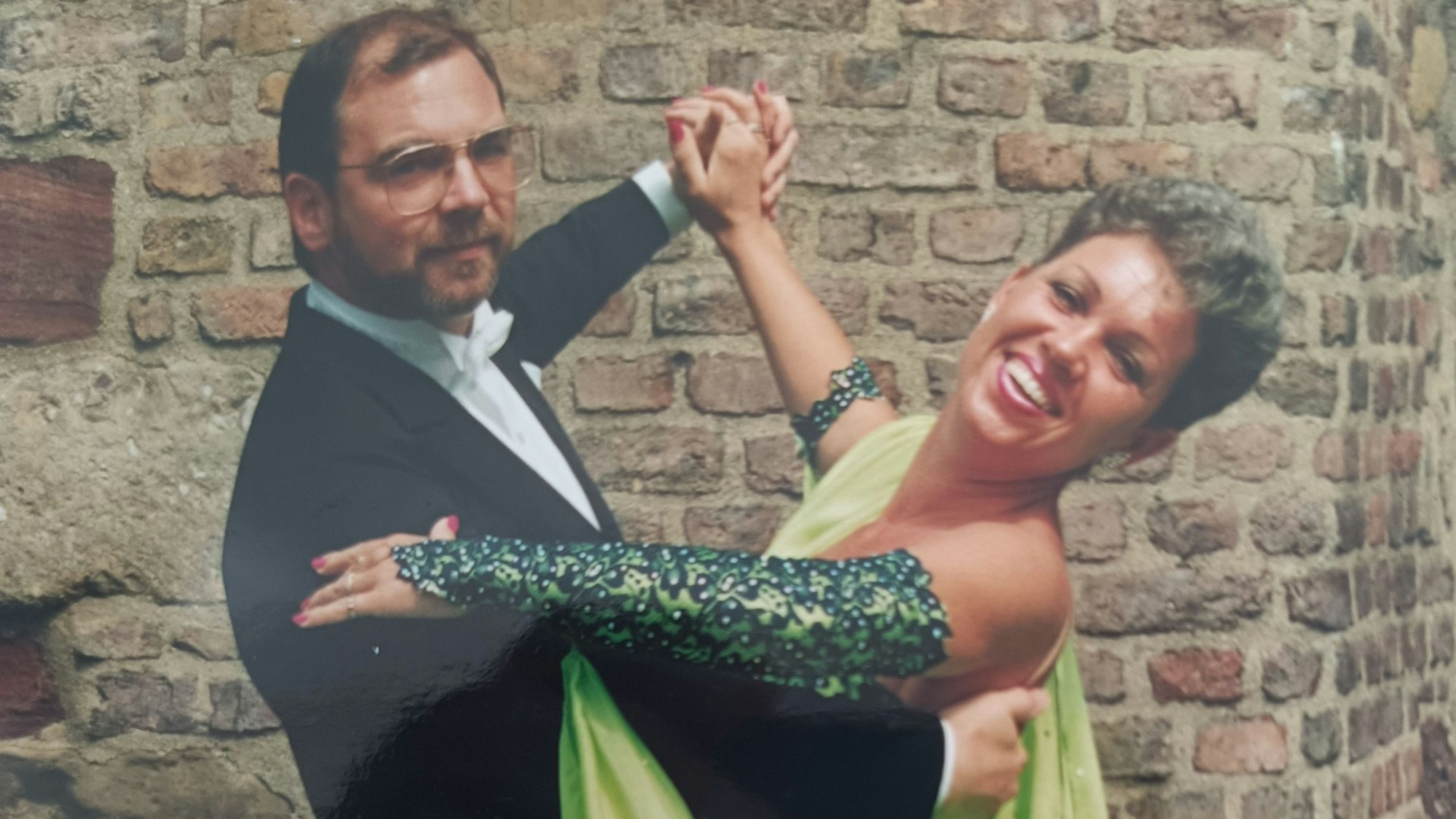 Die beiden tanzen gemeinsam. Jutta Zodet trägt ein grünes Kleid, Ralf Zodet trägt einen Frack und eine eckige Brille.