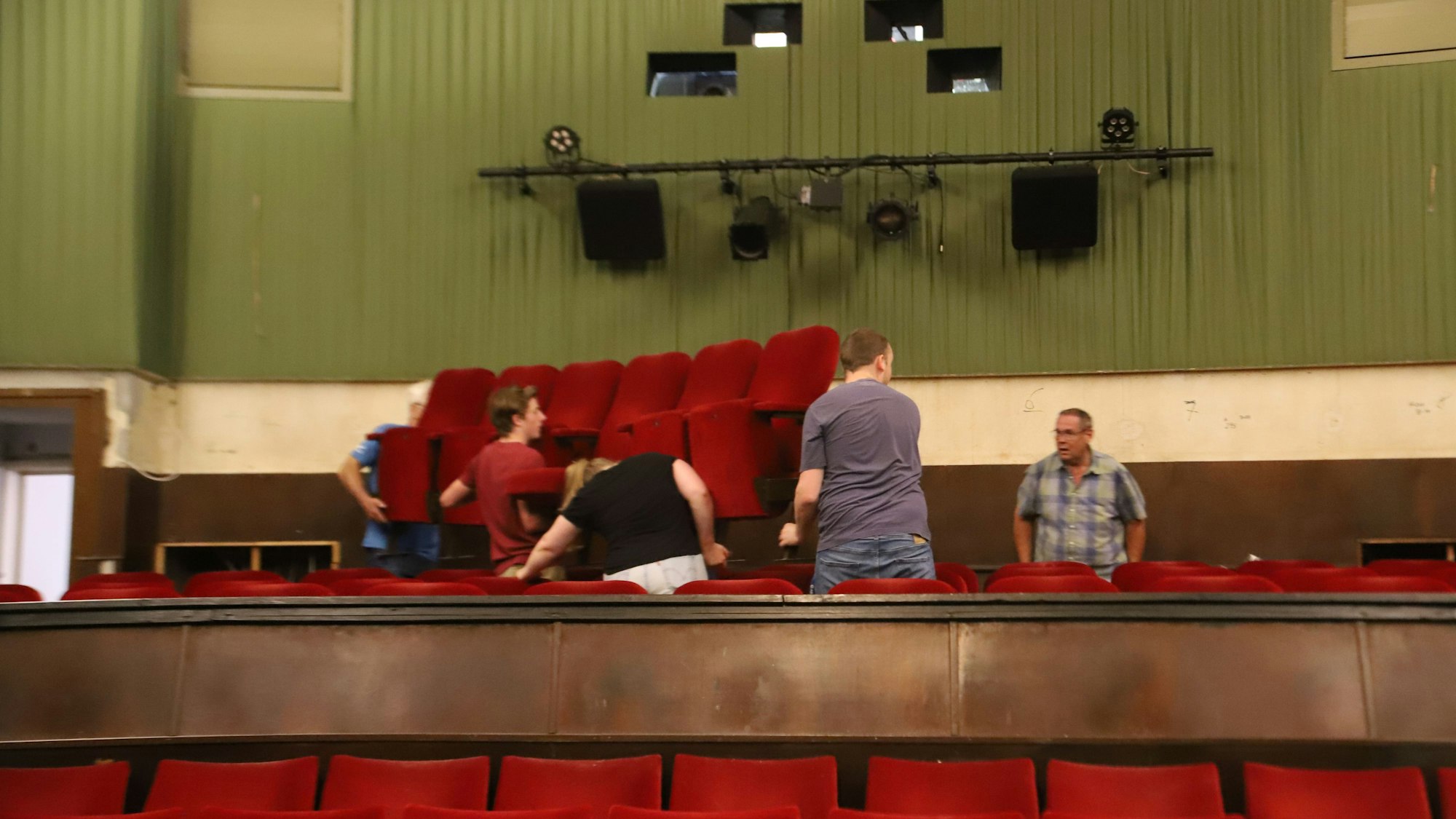 Drei Männer und eine Frau tragen eine Bank mit sechs Kinosesseln.