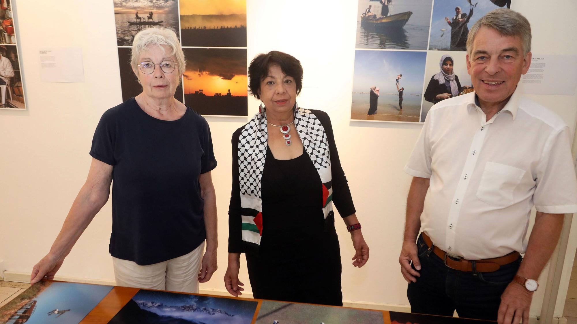 Maria Meiwes-Schmitz, Suraya Hoffmann und Albrecht Schröter stehen vor Fotos, die auf einem Tisch liegen.