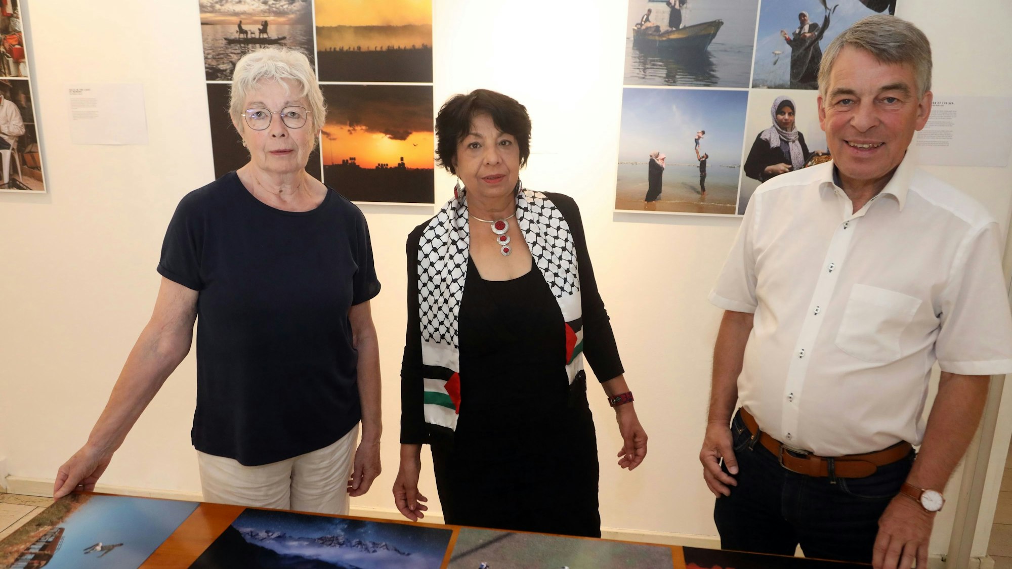 Maria Meiwes-Schmitz, Suraya Hoffmann und Albrecht Schröter stehen vor Fotos, die auf einem Tisch liegen.