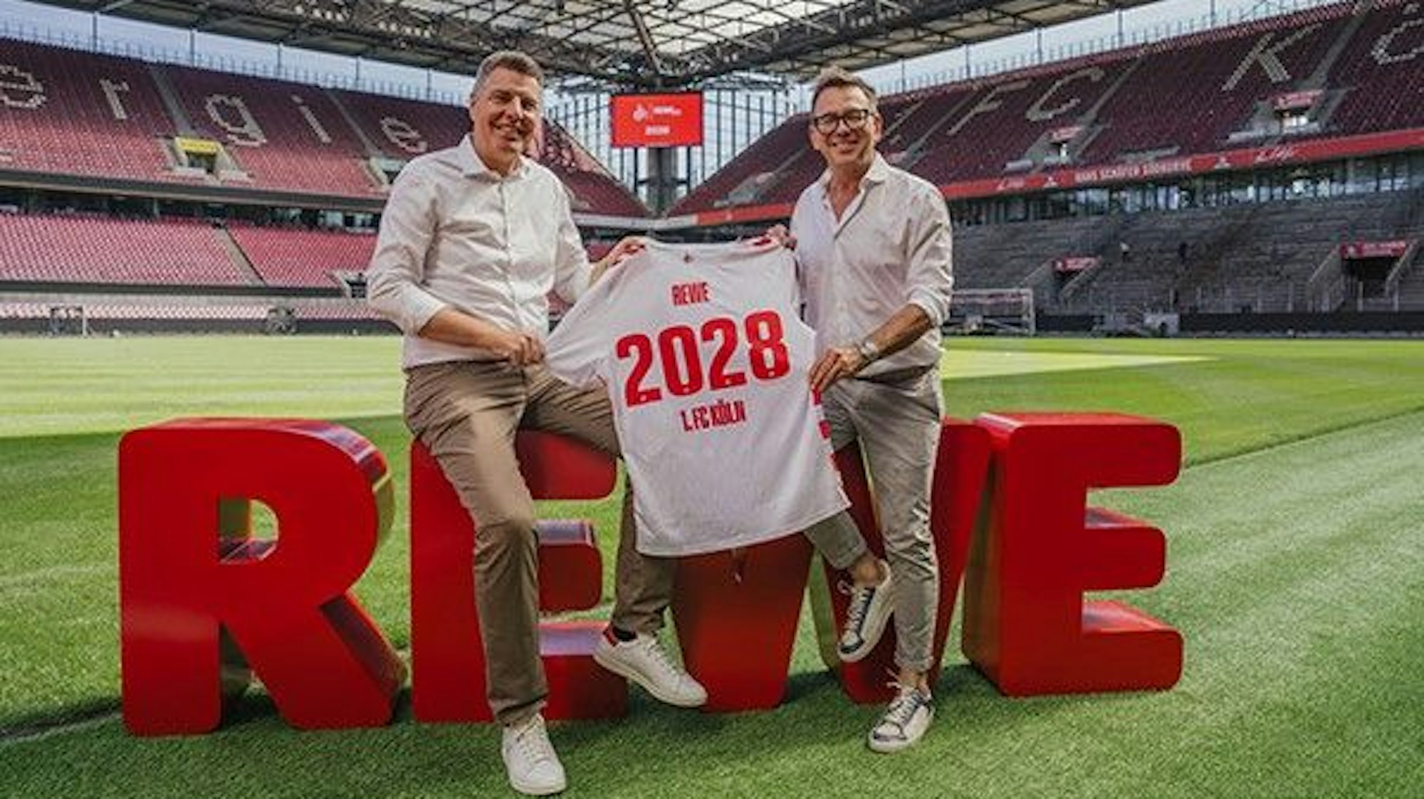 Sven Spork (l.), Bereichsvorstand der Rewe, und Markus Rejek, Geschäftsführer des 1. FC Köln, freuen sich über die weitere Zusammenarbeit und posieren im Rhein-Energie-Stadion für den Fotografen.