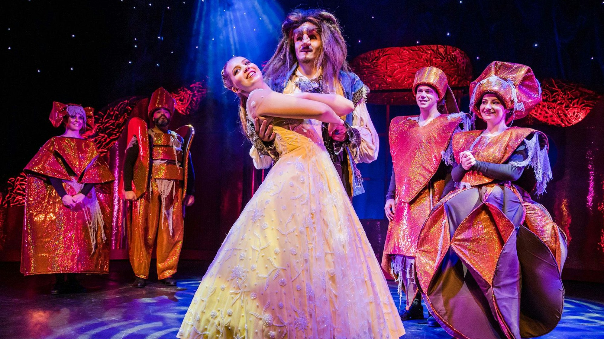 Zu sehen sind Theaterschauspieler auf der Bühne bei einer Aufführung von „Die Schöne und das Biest“.