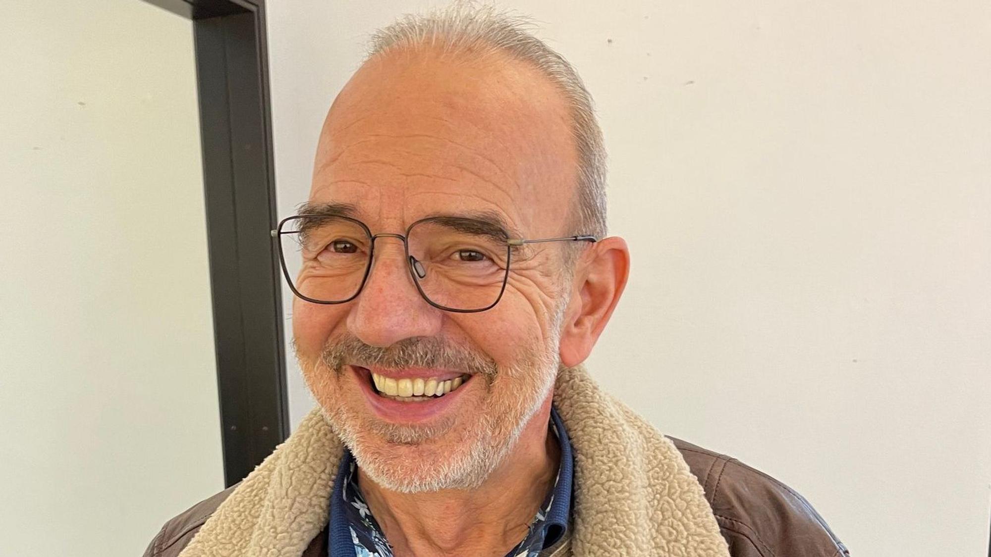 Ein Mann in geöffneter Lederjacke und Pullover lächelt in die Kamera.