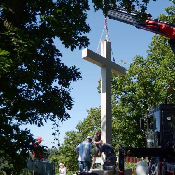 Das Betonkreuz hängt an einem Ladekran. Mitarbeiter der Baufirma bringen es in Position.