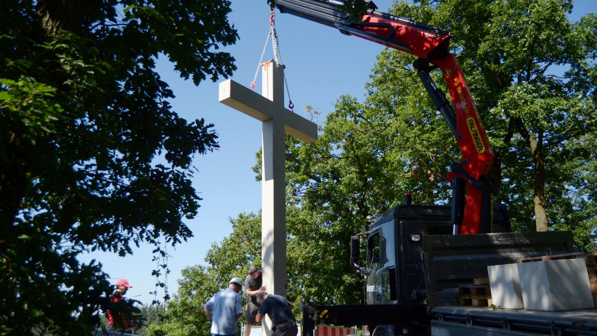 Das Betonkreuz hängt an einem Ladekran. Mitarbeiter der Baufirma bringen es in Position.