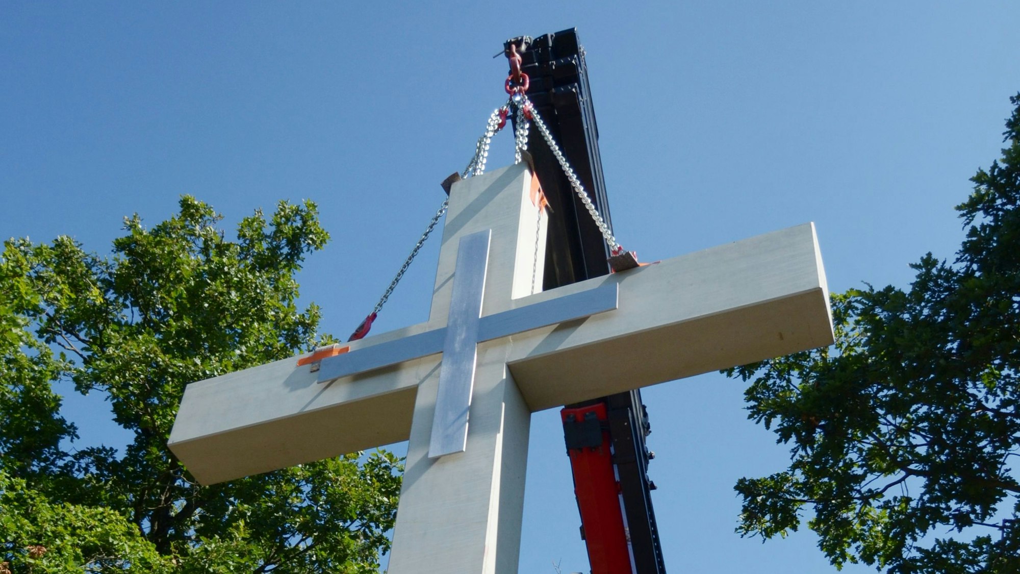 Das Kreuz ist mit Ketten am Kran befestigt. Er bringt es in Position.
