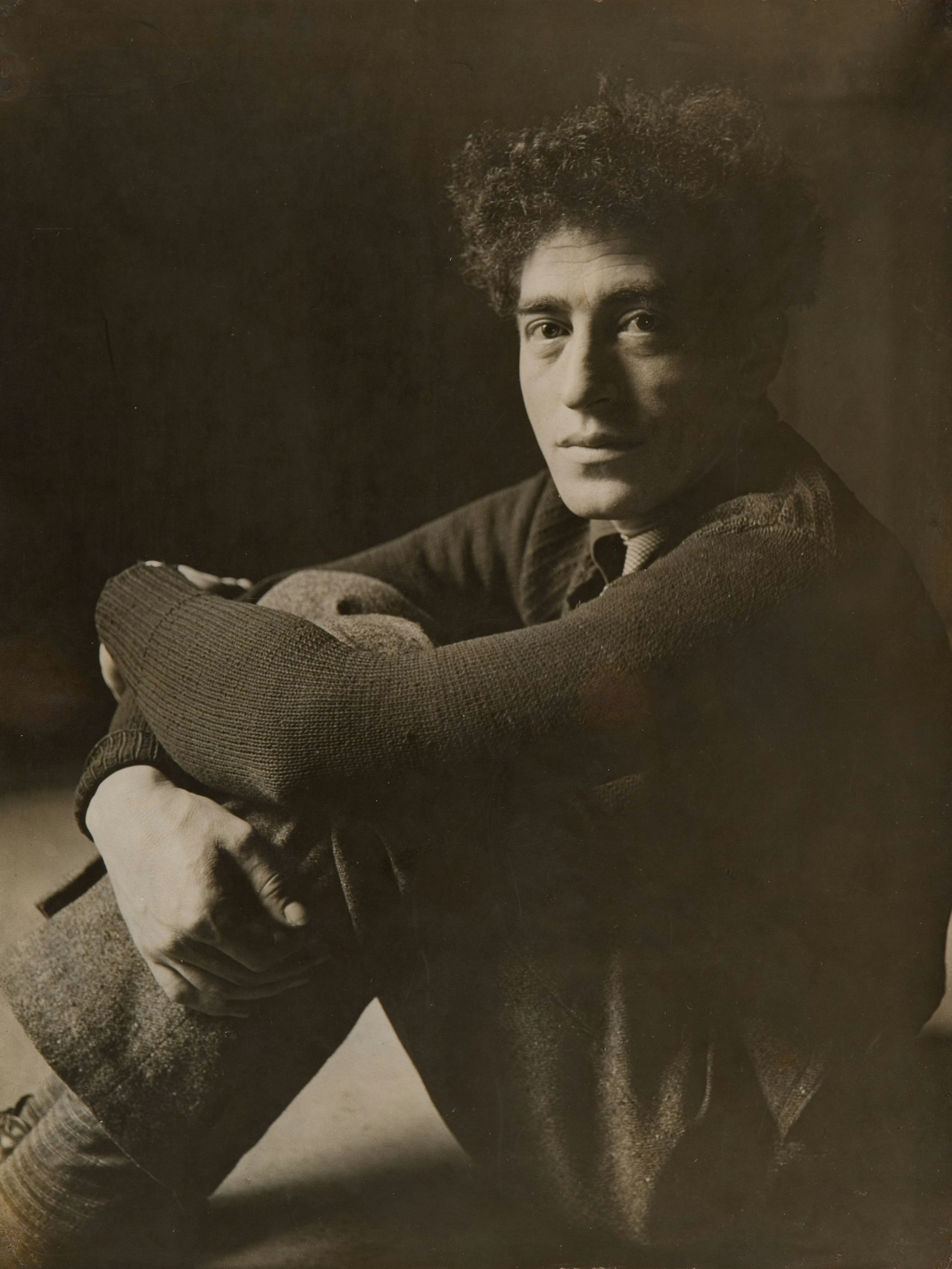 Alberto Giacometti sitzt mit angezogenen Beinen auf dem Boden.