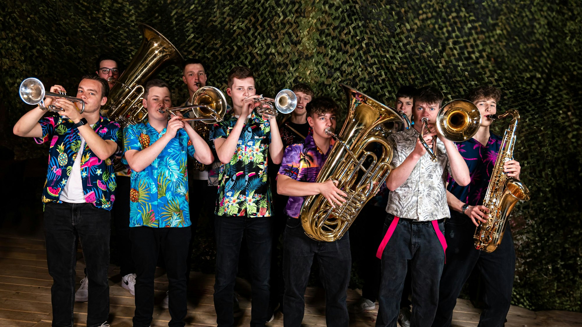 Zehn junge Musiker mit Blechblasinstrumenten stehen in einer Gruppe zusammen und tragen bunte Hawaiihemden.