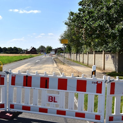 Zu sehen ist ein Absperrzaun an einer Straße.