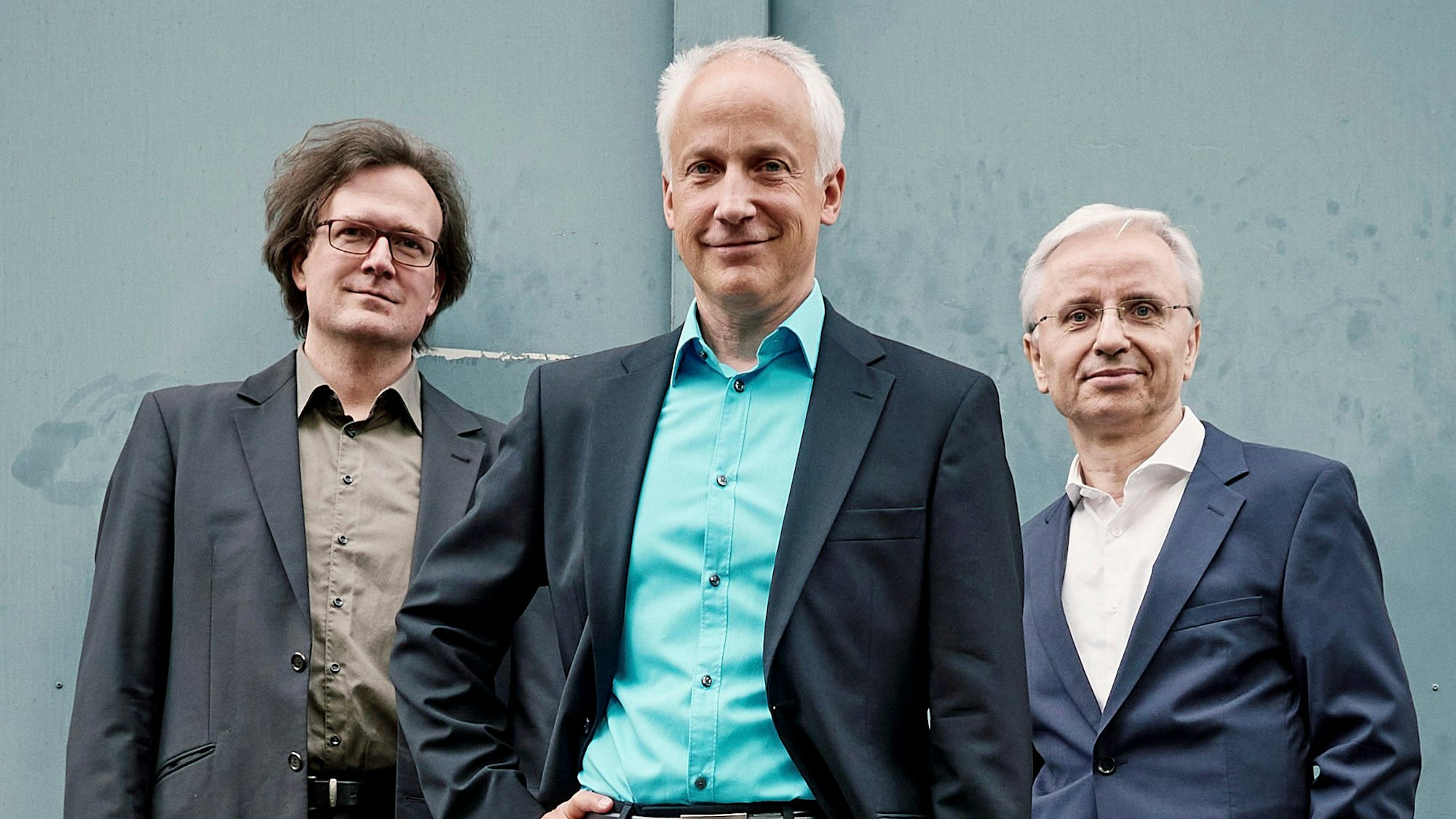 Auf dem Bild sind drei Dozenten der Kunst- und Musikschule im Anzug und mit jeweils unterschiedlichen farbigen Hemden zu sehen.