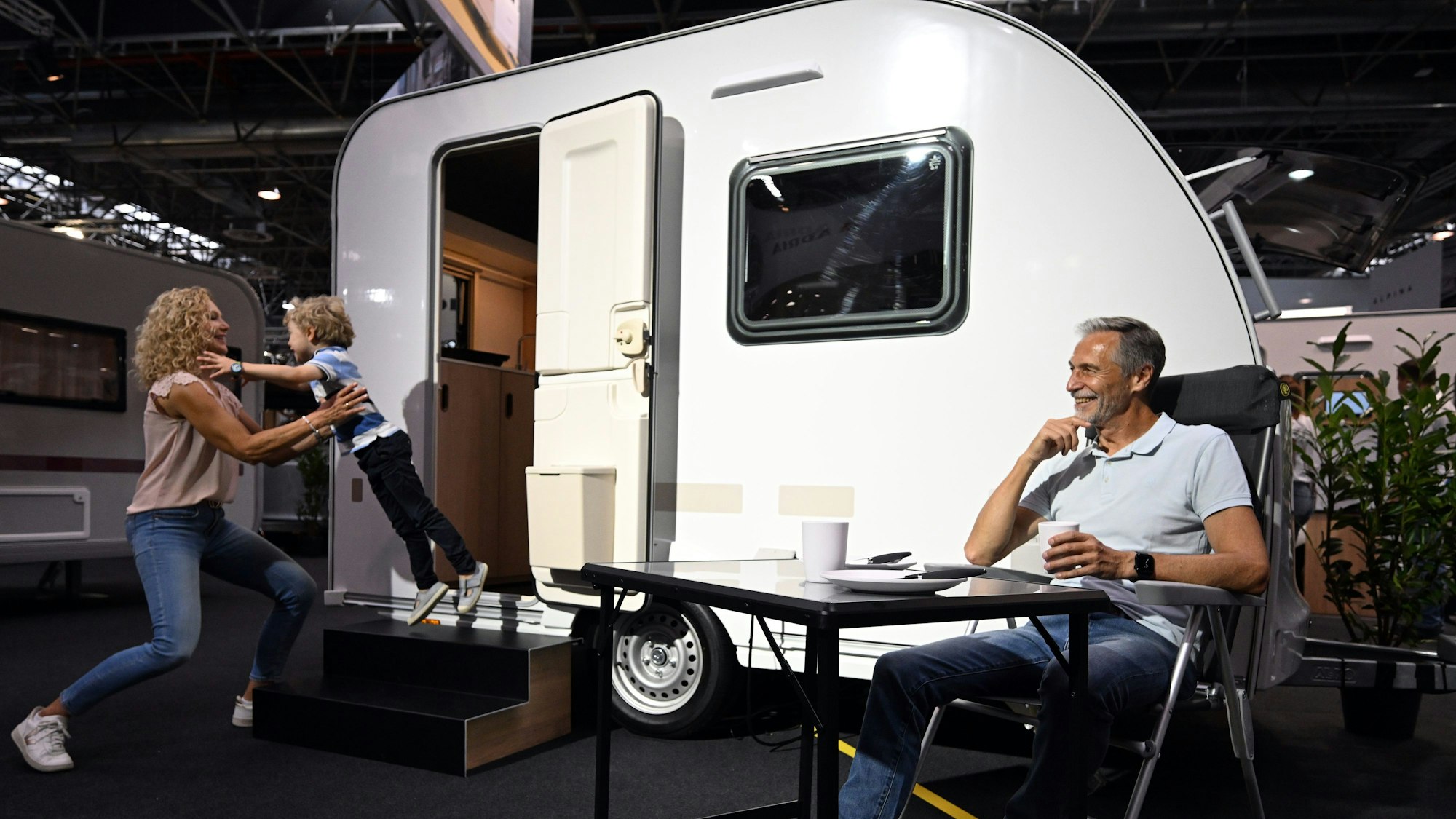 Die Models Anja (l-r), Anton und Andreas stehen und sitzen vor einem Aviva Site 300 LH Mini Caravan der Firma Adria Mobil.