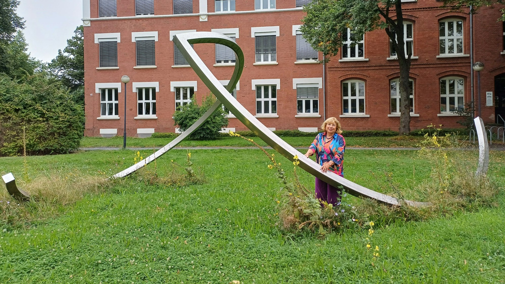 Eine Frau steht an einer Skulptur vor einem Backsteingebäude.