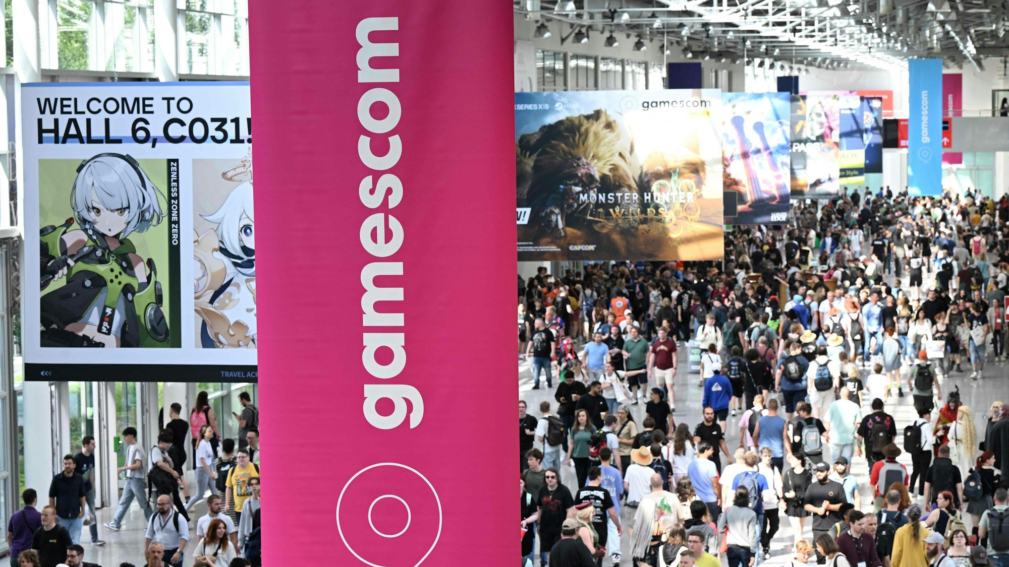 Besucherinnen und Besucher laufen durch die Messe Köln, im Vordergrund ist eine Fahne mit der Aufschrift Gamescom zu sehen.