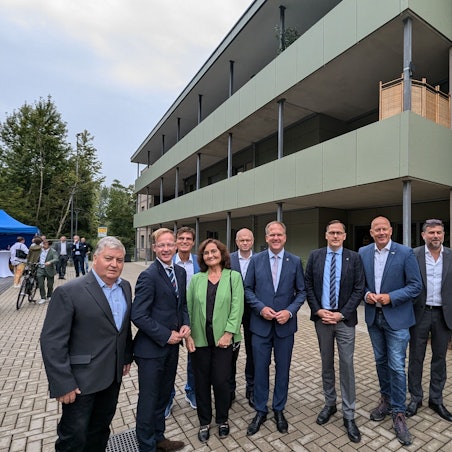 Das Foto zeigt eine Gruppe vor dem Mehrfamilienhaus mit Holzfassade.