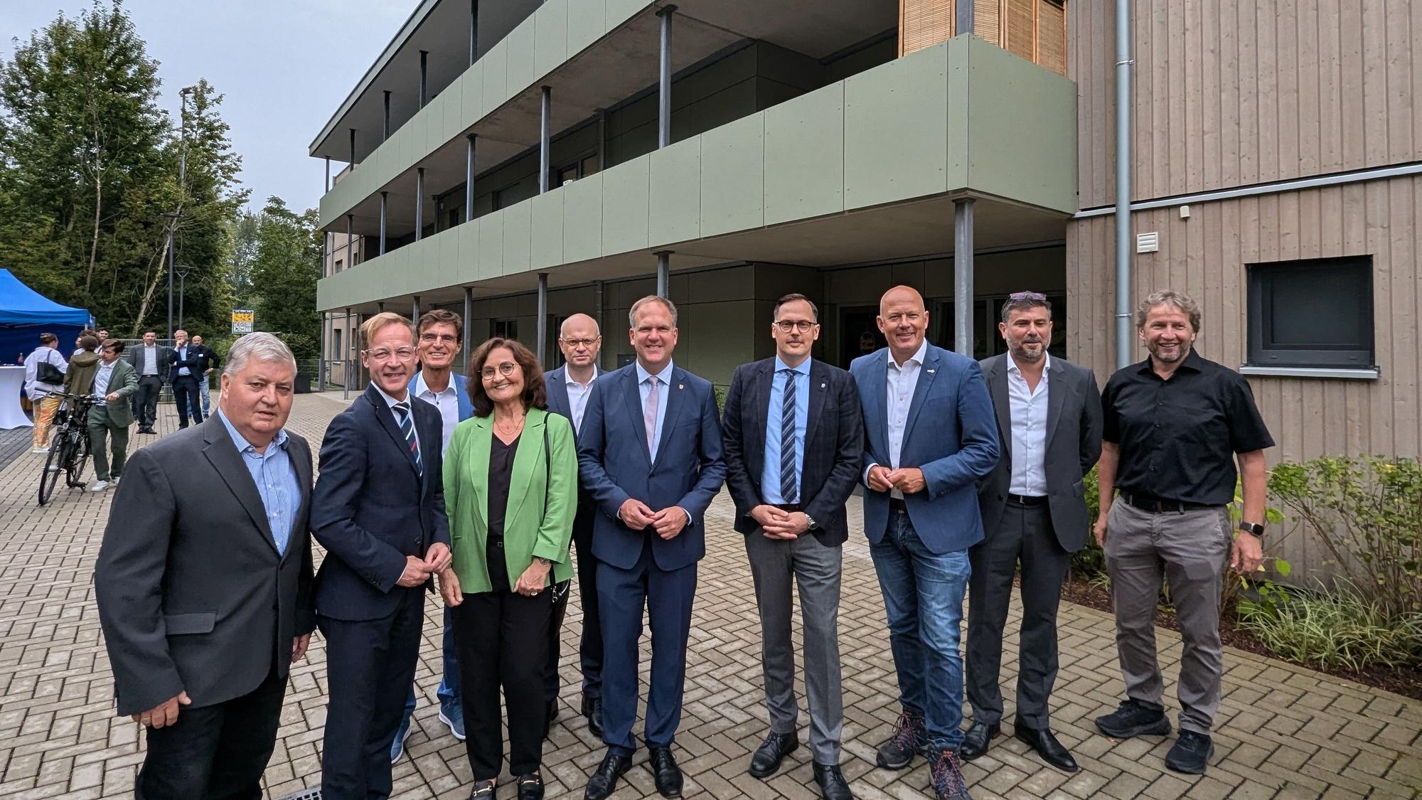 Das Foto zeigt eine Gruppe vor dem Mehrfamilienhaus mit Holzfassade.