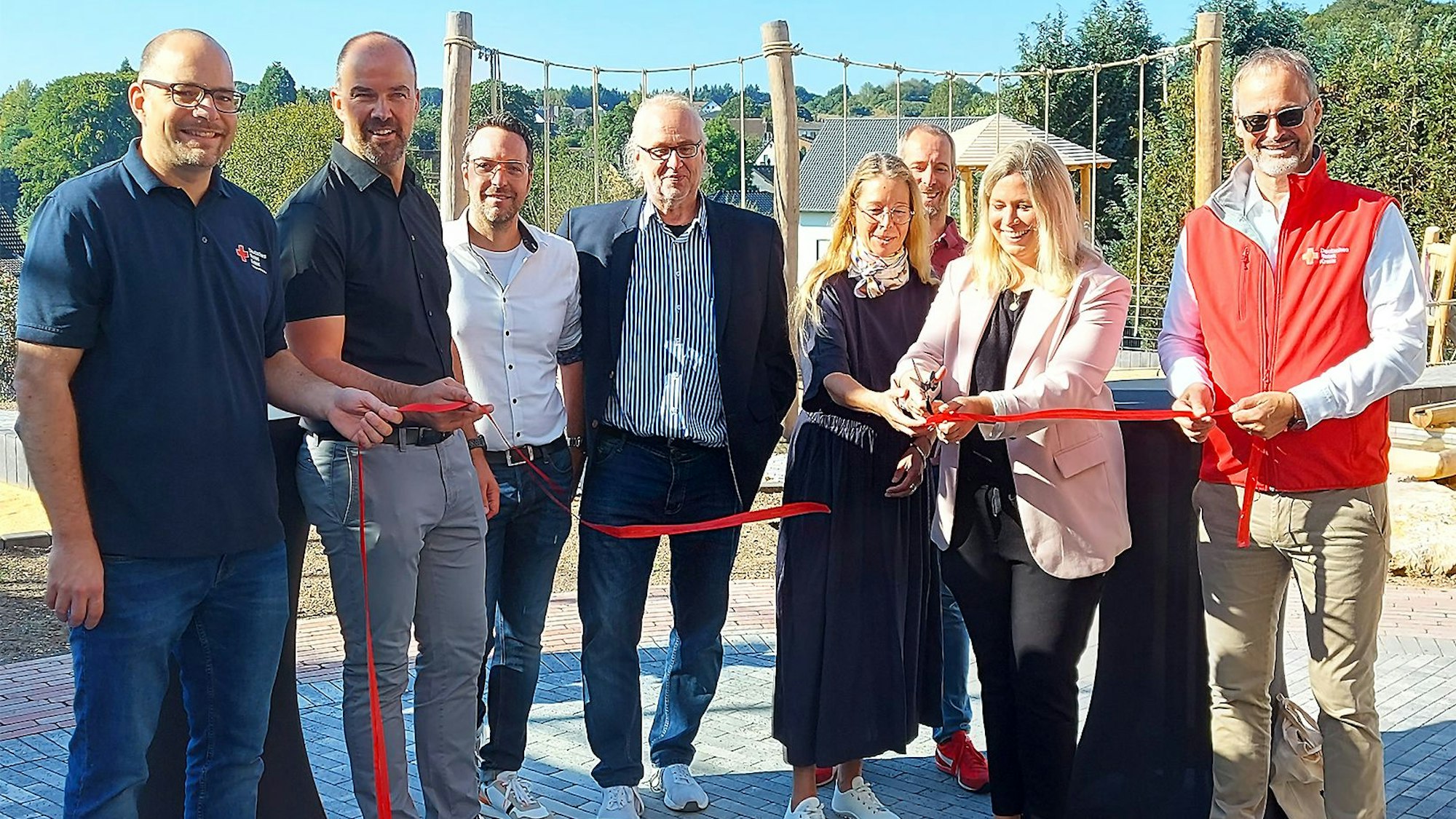 Mehrere Personen stehen bei einem roten Band, das gerade von einer Frau mit einer Schere zerschnitten wird.