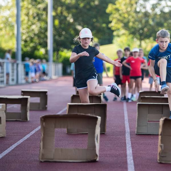 Kinder üben Hürdenlauf mit aufgestellten Pappkartons.