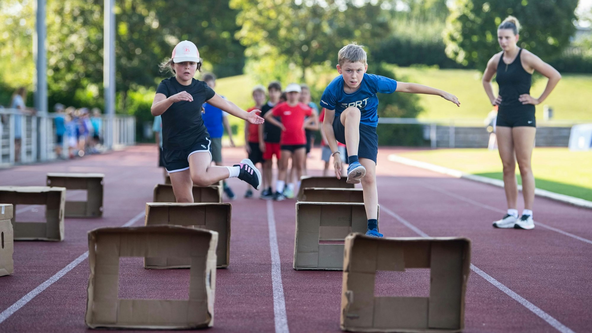 Kinder üben Hürdenlauf mit aufgestellten Pappkartons.