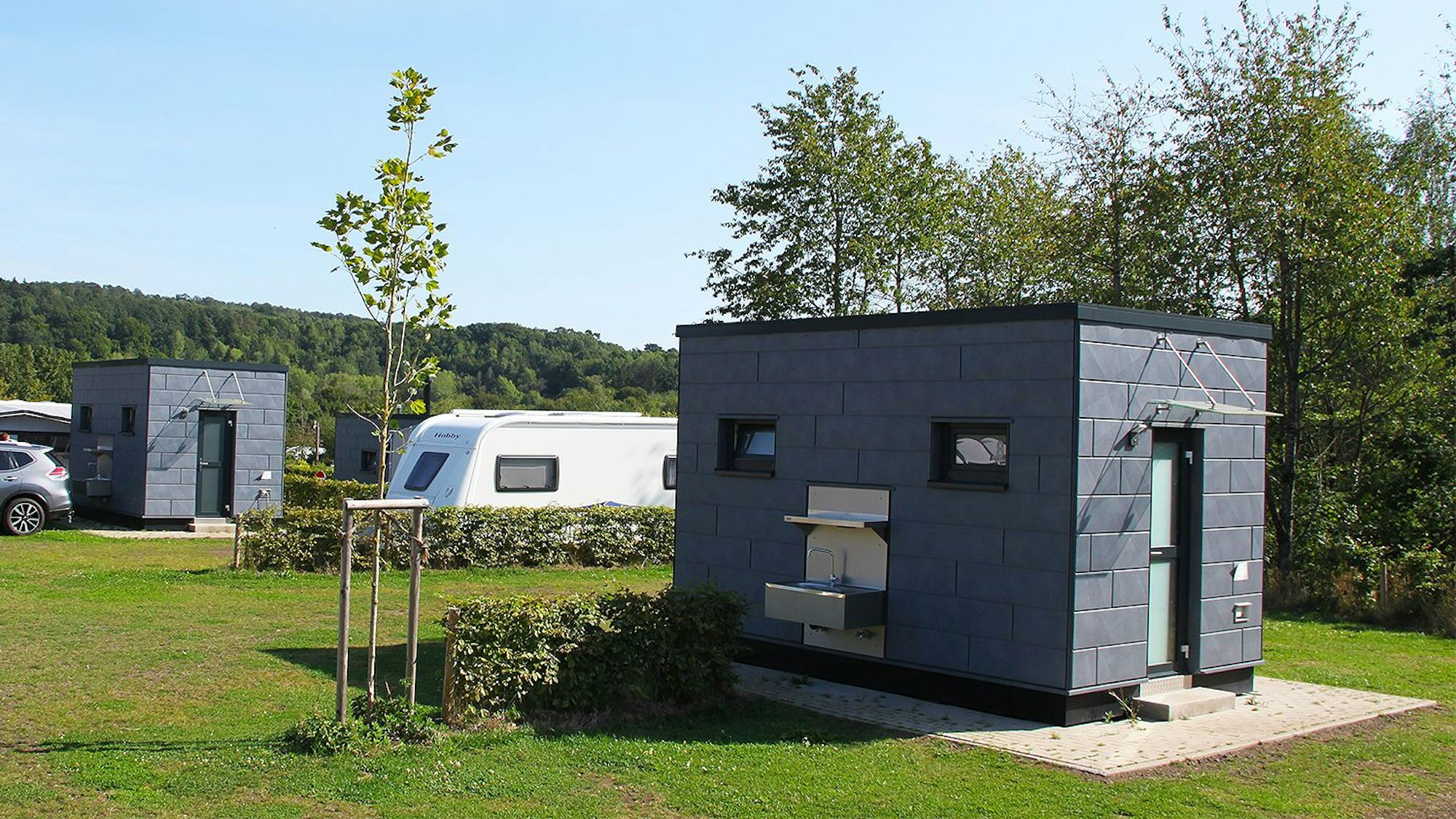 Das Foto zeigt mehrere WC- und Küchenhäuschen, die im Eifel Camp verteilt sind.