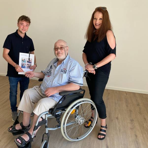 Philip Wiskirchen übergibt einen Schlüssel an Heinz Kesten, der im Rollstuhl sitzt. Kümmerin Anuschka Schwinning-Hess steht daneben.