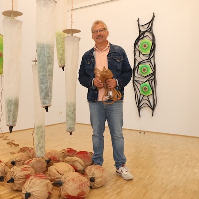 Der Künstler steht neben hängenden Objekten.