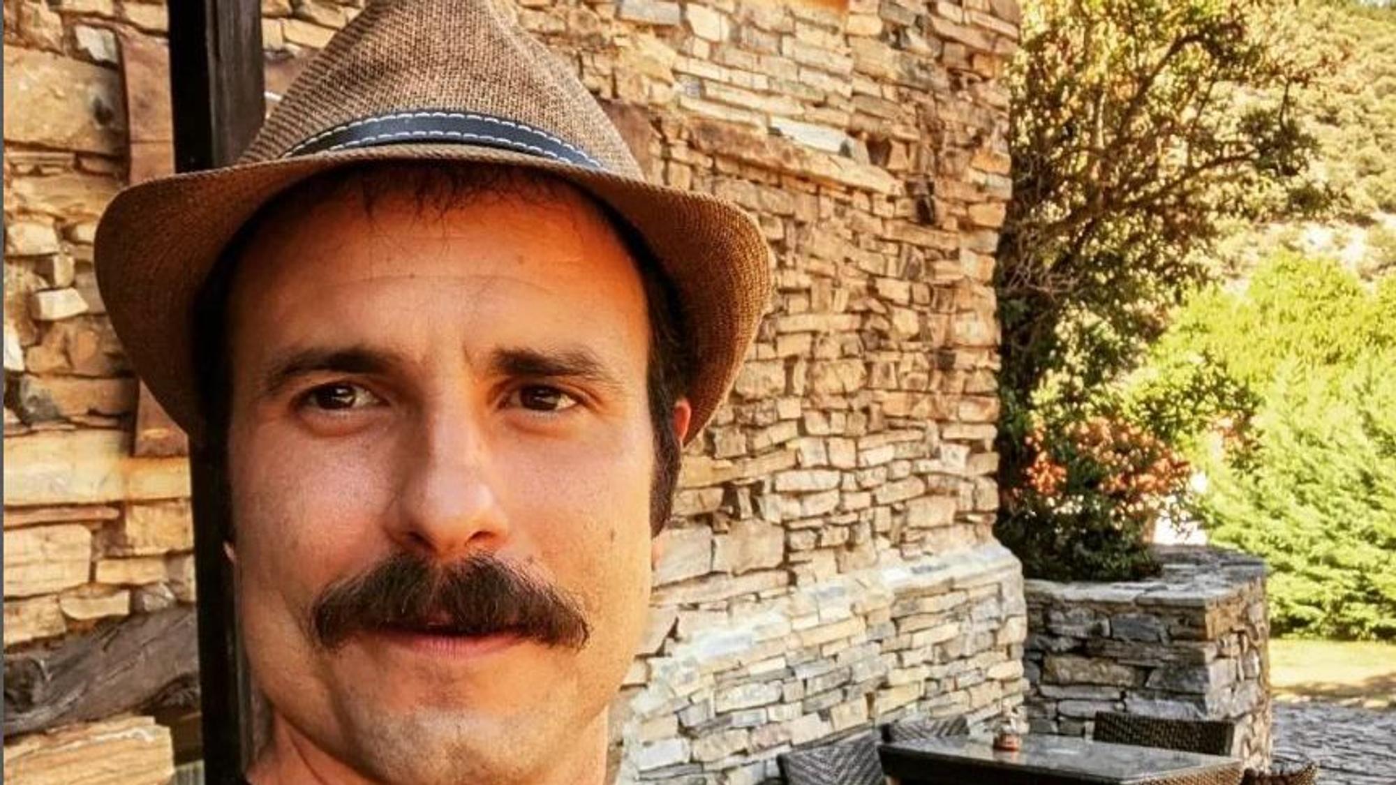 Julián Ortega sitzt vor einer Mauer und lacht.