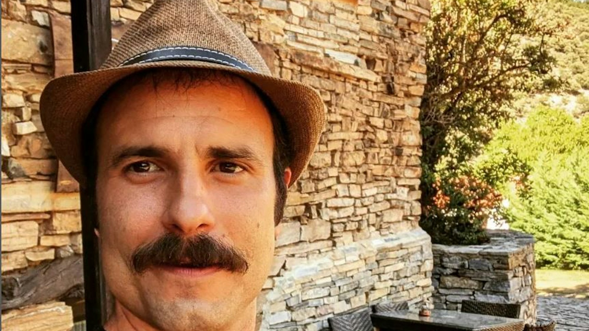 Julián Ortega sitzt vor einer Mauer und lacht.