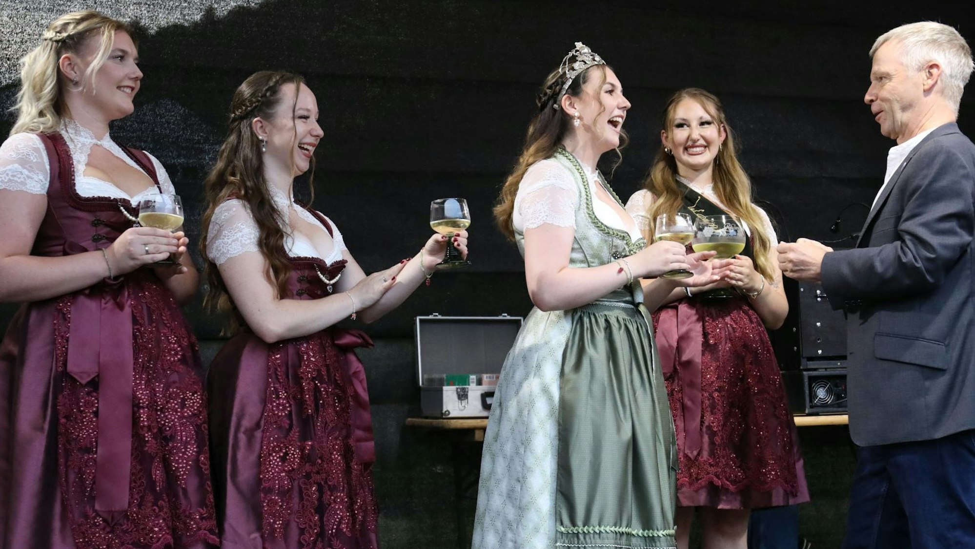 Vier junge Frauen in rotem beziehungsweise grünem Kleid mit einem Mann auf einer Bühne.