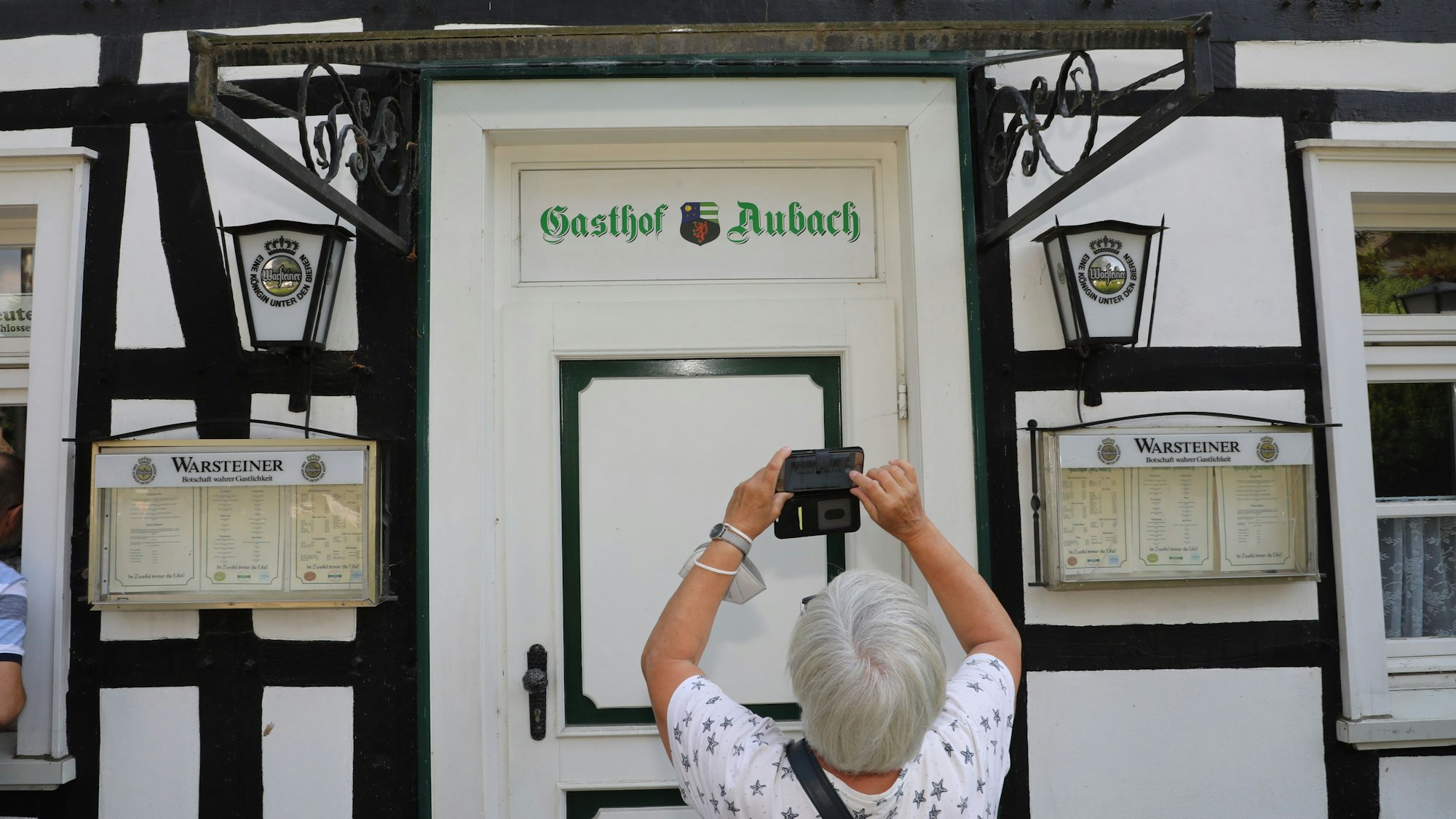 Eine Frau fotografiert den Schriftzug über der Tür des TV-„Gasthof Aubach“ in Kürten-Olpe.