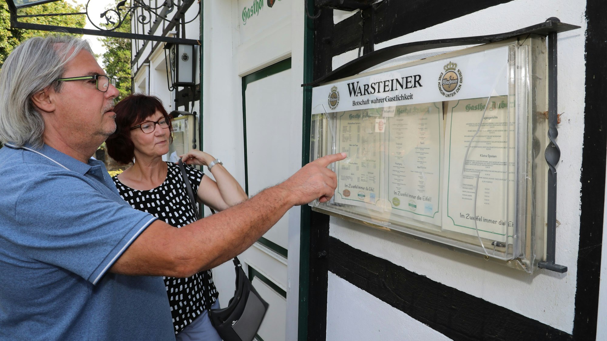 Ein Paar schaut auf die Speisekarte im Aushang des TV-„Gasthof Aubach“ in Kürten-Olpe.