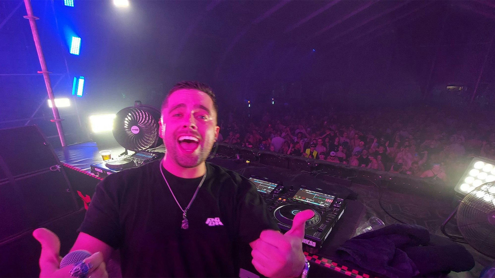 Das Bild zeigt DJ Aversion, der in die Kamera schaut. Hinter ihm ist eine feiernde Masse zu erahnen.