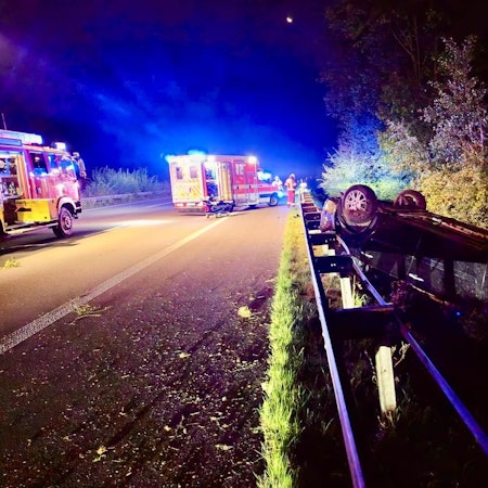 Ein Auto liegt neben der Autobahn hinter der Leitplanke.