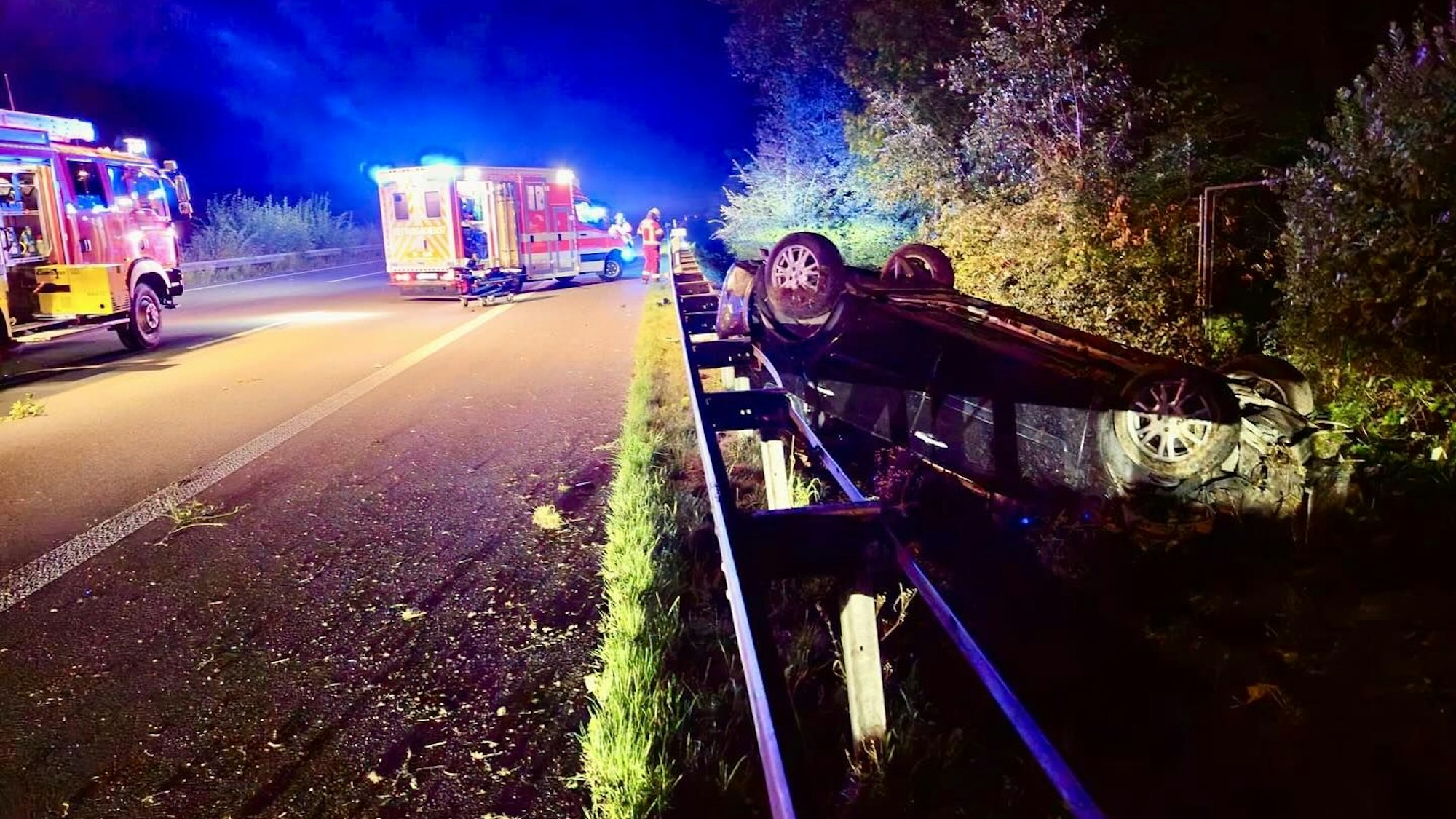 Ein Auto liegt neben der Autobahn hinter der Leitplanke.
