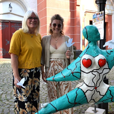 Drei Frauen und eine bunte Pappmaché-Figur im Stil der Nanas von Niki de Saint-Phalle.