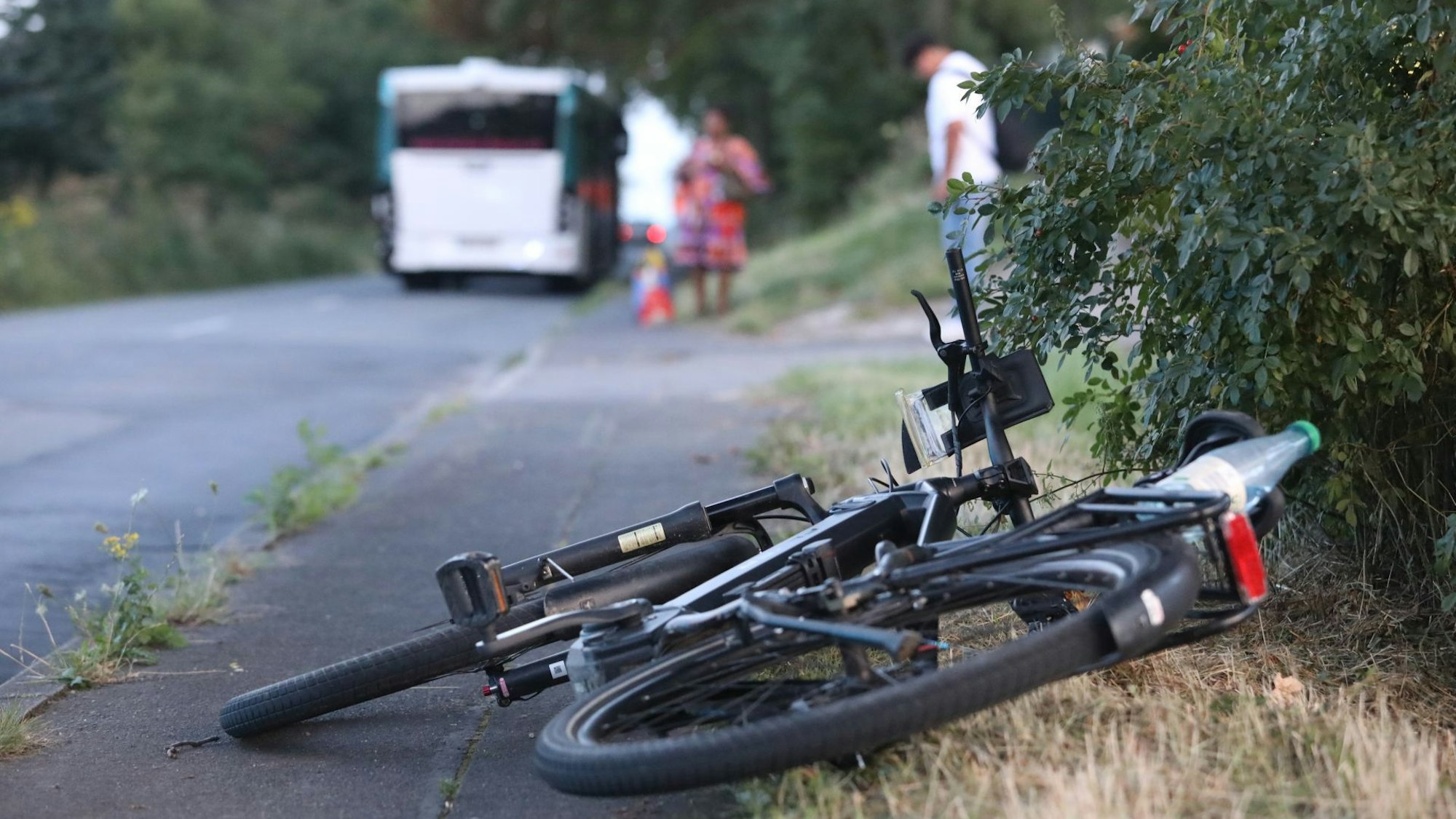 Ein Fahrrad liegt auf der Seite an einer Straße, im Hintergrund ist ein Bus zu sehen.