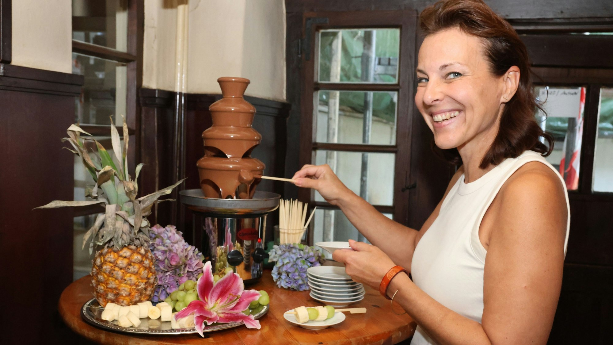 Eine Frau taucht einen Spieß in den Schokobrunnen.