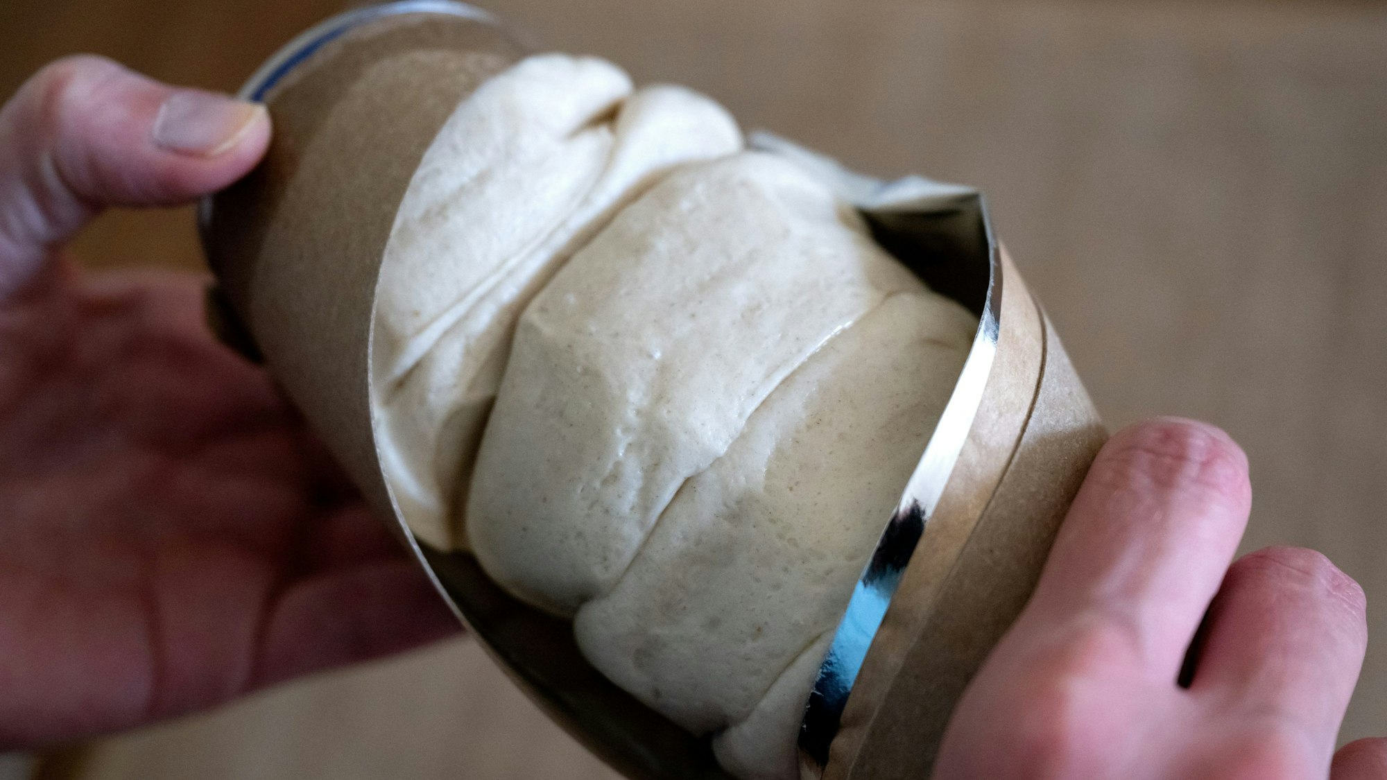 Eine Frau öffnet in einer Küche eine Dose mit Teig für Aufbackbrötchen.